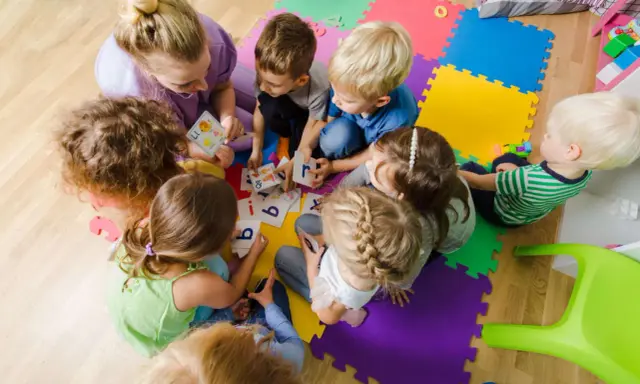 Dzieci i nauczycielka bawią się kartami z literami, ucząc się alfabetu. Ciekawe zajęcia w przedszkolu.