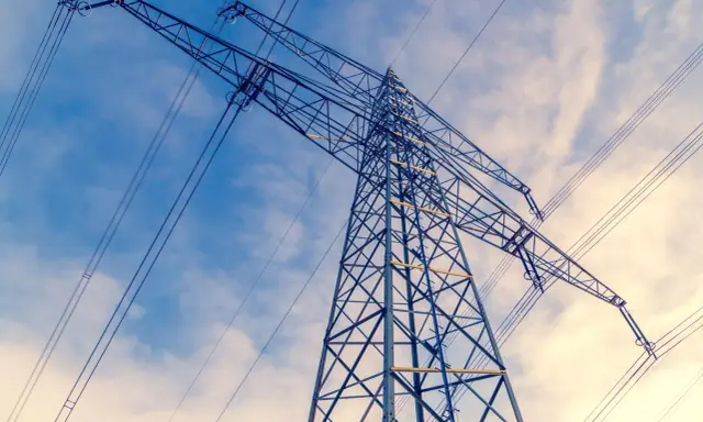 Wysoki słup energetyczny z liniami przesyłowymi na tle błękitnego nieba z chmurami. Linie te, niczym niewidzialne ley lines, niosą energię.