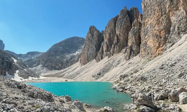 Il **lago di Antermoia**, incastonato tra imponenti pareti rocciose, brilla di un turchese intenso sotto un cielo azzurro.