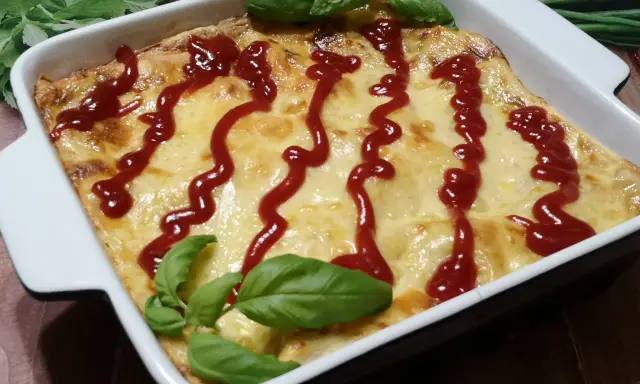 Pyszne, zapieczone fit lasagne w białym naczyniu, polane ketchupem i ozdobione listkami bazylii.