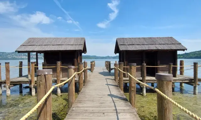 Pontile in legno con due capanne sul lago di Viverone, sotto un cielo azzurro con nuvole bianche.