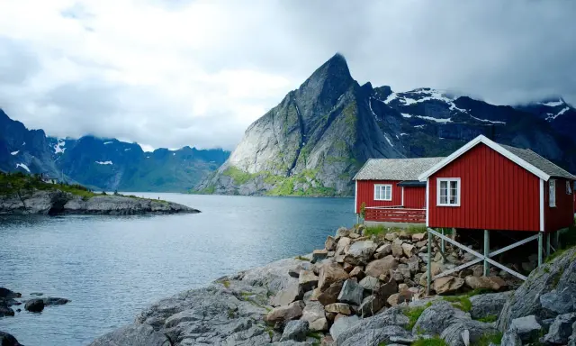 Två röda stugor vid en sjö med dramatiska berg i bakgrunden. Perfekt för att vandra i Norge.