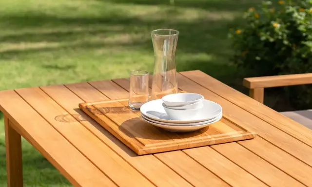 Vacker teakmöbel som behöver behandlas för att behålla sin lyster. Tallrikar, skålar och glas står redo för en utomhusmåltid.