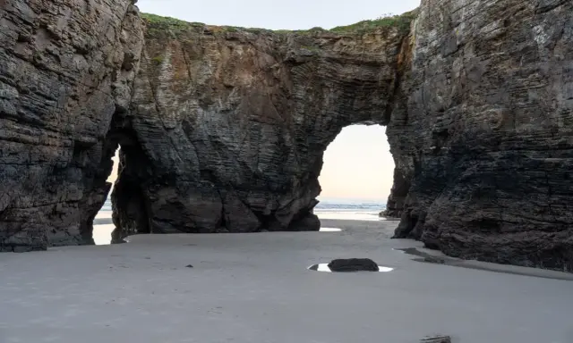 Felsbögen am Praia das Catedrais, die wie Kathedralen wirken, mit Sand und Meer im Hintergrund.