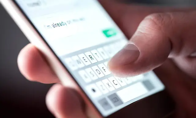 Palec pisze na klawiaturze telefonu, tworząc wiadomość. Widać fragment tekstu "I'm already on my way" i klawisze z literami. To klasyczny przykład polskie znaki w sms.