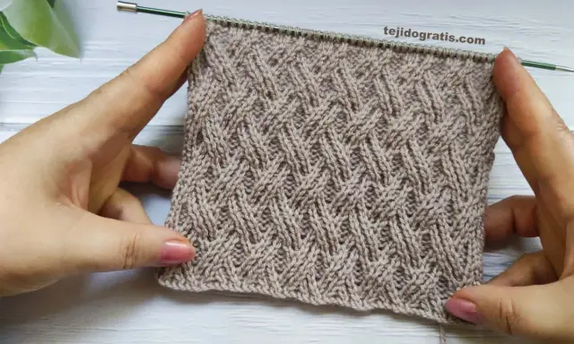Manos sostienen un tejido cruzado de lana beige con un patrón de rombos entrelazados.