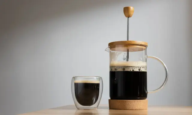 Frisch gebrühter Kaffee mit Wasser in einer French Press und einem Glas. Der Duft von Kaffee liegt in der Luft.