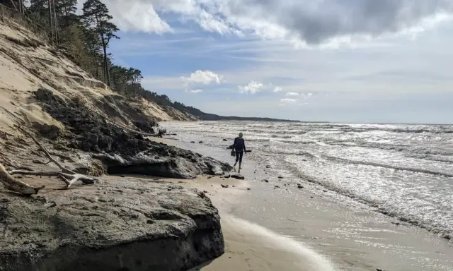 Spacerująca osoba na plaży w Ustce, w oddali widać orzechowo-brązowe klify.