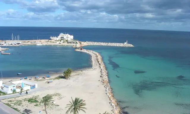 Piękna plaża i turkusowe morze w Tunezji. Październikowa pogoda sprzyja spacerom brzegiem, gdzie widać białe budynki i palmy.