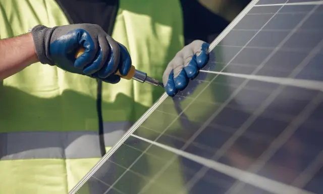 Mains nues, gants bleus et jaunes, tournevis en action pour la réparation d'un panneau solaire.