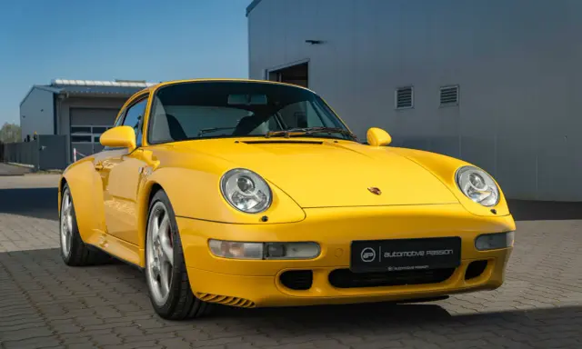 Gelber Porsche 993 vor einem modernen Gebäude. Die Wertentwicklung dieses Klassikers ist bemerkenswert.