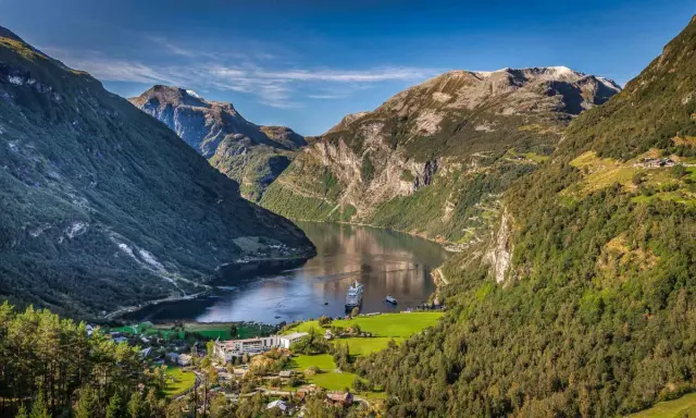 Majestätische norwegen fjorde mit einem Kreuzfahrtschiff, das auf dem ruhigen Wasser fährt. Grüne Berghänge und ein kleines Dorf am Ufer.