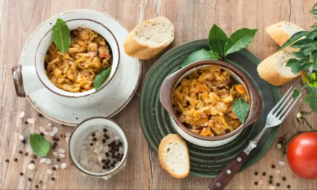 Dwa naczynia z aromatycznym bigosem z młodej kapusty, podane z pieczywem, pomidorem i przyprawami.