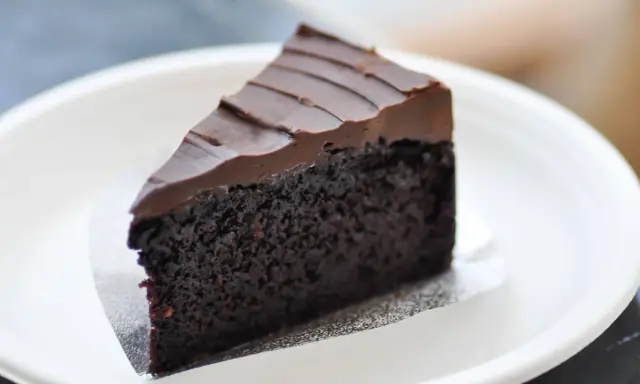 Una fetta di torta al cioccolato senza burro, soffice e ricoperta da glassa al cioccolato, servita su un piatto bianco.