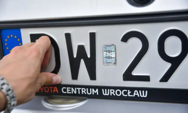 Dłoń dotyka polskiej tablicy rejestracyjnej z literami DW i cyframi 29.