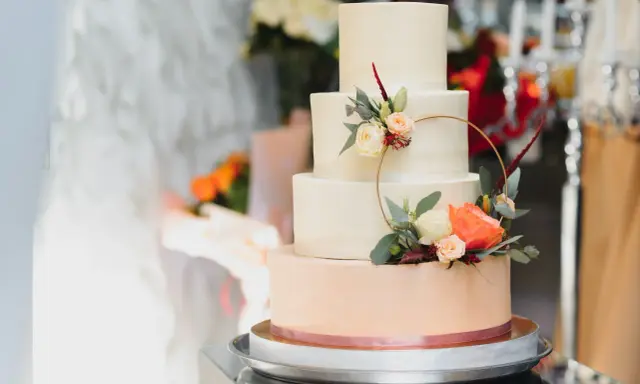 Czteropiętrowy tort weselny w pastelowych kolorach, ozdobiony świeżymi kwiatami i złotym pierścieniem. To najmodniejsze najpiękniejsze torty weselne.