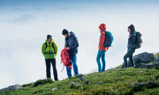 Cztery osoby w kolorowych kurtkach i plecakach na tle nieba. To właśnie **outdoor**, czyli aktywność na świeżym powietrzu.