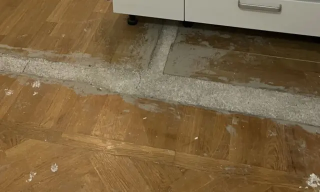 Arbete pågår för att ta bort laminatgolv. Ett vitt pulver och grått material syns på det gamla trägolvet.