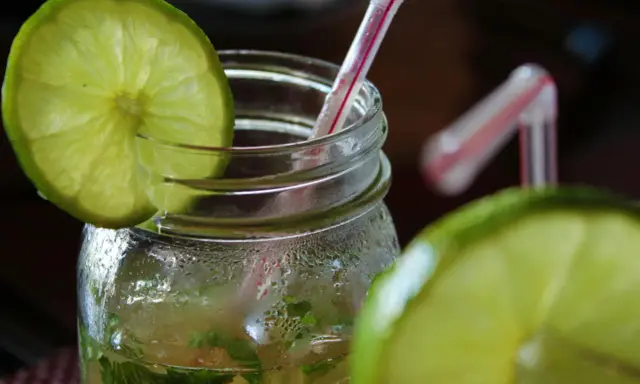 Orzeźwiający mohito drink, z widocznymi składnikami: limonką i miętą, w szklanym słoiku z rurką.