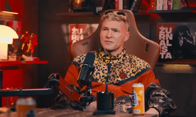 Mężczyzna w kurtce w panterkę, z blond włosami, siedzi w fotelu. Na półce za nim figurki Iron Mana. Wiek majora SPZ.