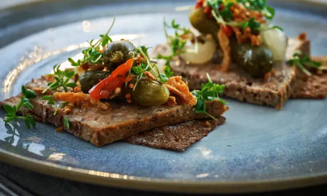 Två bitar mörkt bröd med leverpastej, toppade med cornichoner, chili och krispiga topping. Ett enkelt leverpastej recept att inspireras av.