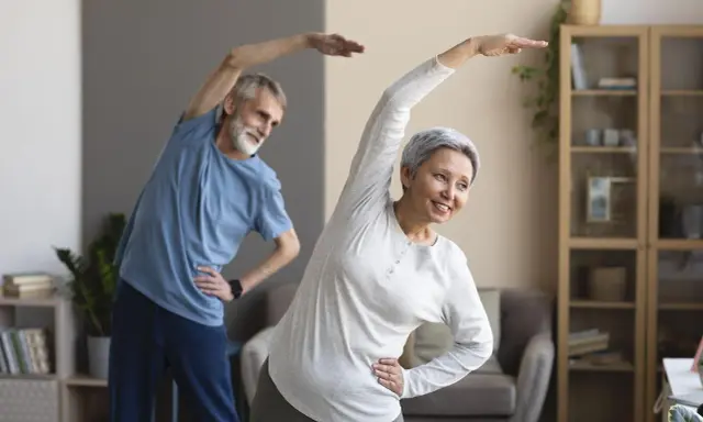 Uśmiechnięta para seniorów ćwiczy w domu. Aktywne zajęcia dla seniorów to świetny sposób na zdrowie i dobre samopoczucie.