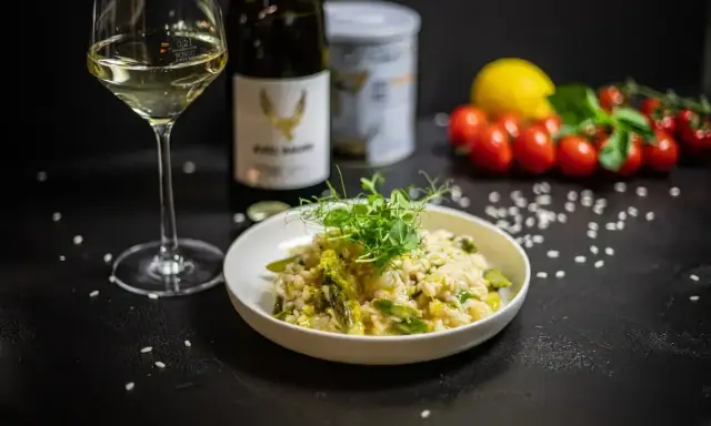 Aksamitne risotto z kurczakiem i szparagami, udekorowane kiełkami. Obok kieliszek białego wina i butelka.