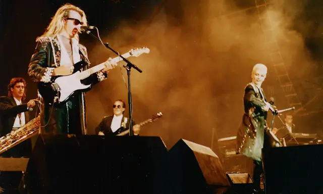 Medlemmar av Eurythmics på scen. Dave Stewart spelar gitarr, Annie Lennox sjunger. En saxofonist och en keyboardist syns också.