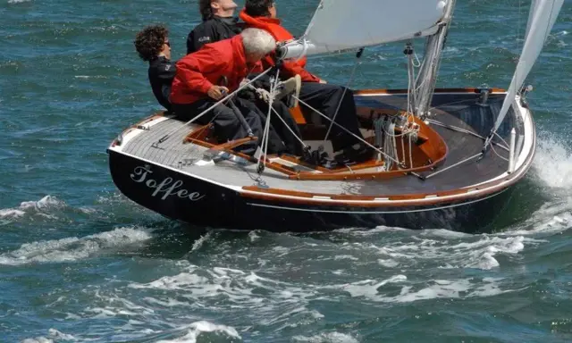 Le voilier "Toffee" navigue sur une mer agitée, quatre personnes à bord profitent de la balade.