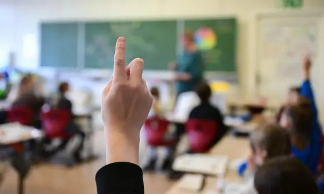 Ein Finger zeigt nach oben im Klassenzimmer. Dies symbolisiert die **Schulpflicht in Deutschland**, wo Kinder lernen und Fragen stellen.