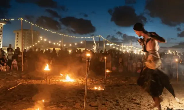Spettacolo di fuoco sulla spiaggia di Rimini, estate. Artista si esibisce tra torce e fuochi d'artificio, con pubblico e luci in lontananza.