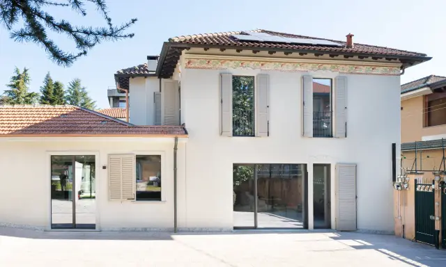 L'abbinamento colori facciata e serramenti crea un'armonia moderna. La casa bianca con dettagli decorativi si fonde con le persiane e gli infissi grigio chiaro.