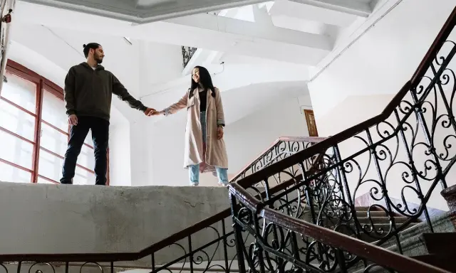 Pareja tomados de la mano en una escalera, ¿qué es ser posesivo? Él la mira, ella sonríe.