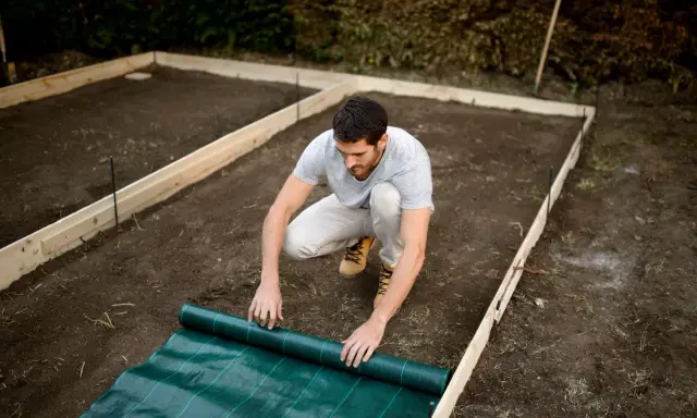 Hombre desplegando tela verde sobre el terreno preparado para una solera de hormigón.