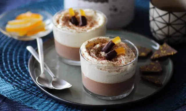 Deux verrines 3 chocolat, garnies de crème fouettée, de copeaux de chocolat et d'écorces d'orange confites.