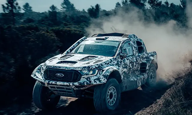 Un Ford Raptor Dakar camuflado levanta polvo en un terreno agreste.