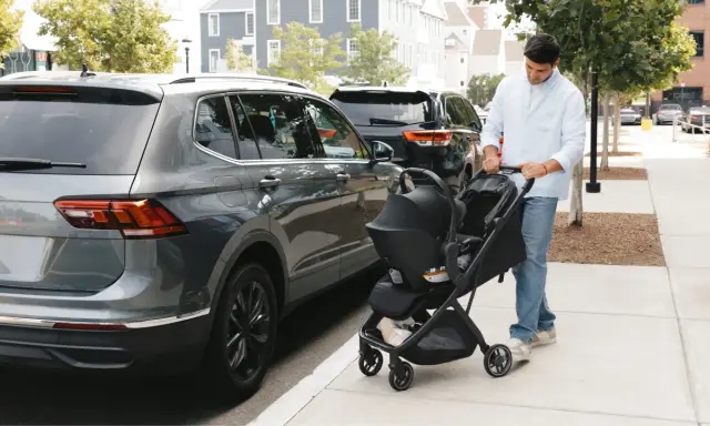 Hombre empuja un cochecito con un sistema sujeción infantil silla coche, junto a un coche gris.