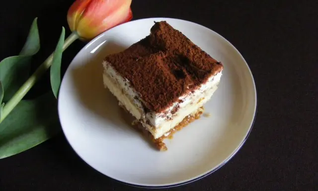 Pyszny kawałek tiramisu, jednego z 10 ciast bez pieczenia, obok czerwonego tulipana.