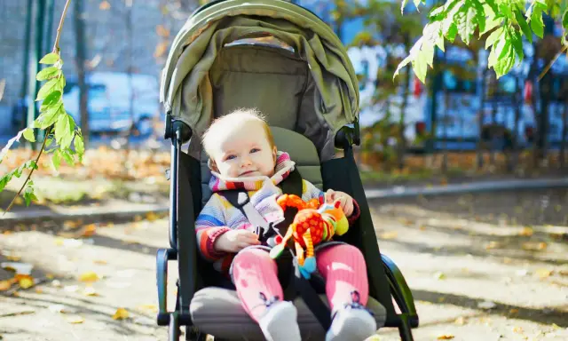 Uśmiechnięte dziecko w kolorowym sweterku siedzi w spacerówce, trzymając zabawkę.