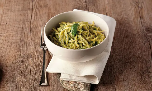 Un piatto invitante di trofie al pesto, guarnito con una foglia di basilico, su un tavolo di legno rustico.