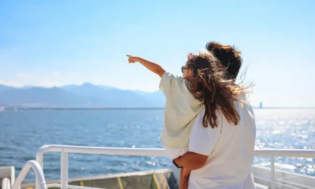 Bambina indica l'orizzonte da una nave, con la famiglia in vacanza a Favignana. Il mare azzurro e le montagne sullo sfondo creano un'atmosfera serena.