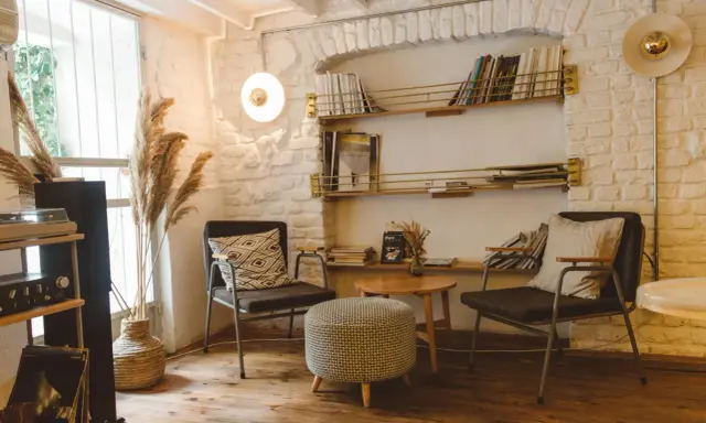 Acogedor rincón de lectura con sillas cómodas, mesa auxiliar, estanterías llenas de libros y plantas secas.