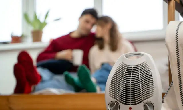 Pareja acurrucada con bebidas calientes, un radiador eléctrico en primer plano. Así funciona un radiador eléctrico para calentar el hogar.