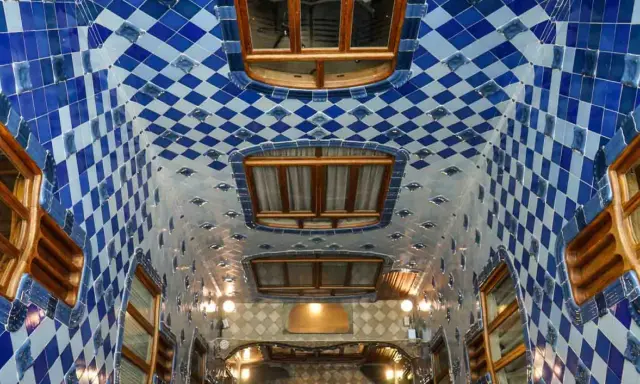 Interno della Casa Batlló: soffitto ondulato con piastrelle blu e bianche a rombi, finestre in legno e luci soffuse.
