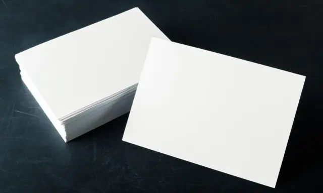 Pila de tarjetas blancas sobre fondo oscuro. El gramaje del papel es ideal para impresiones de alta calidad.