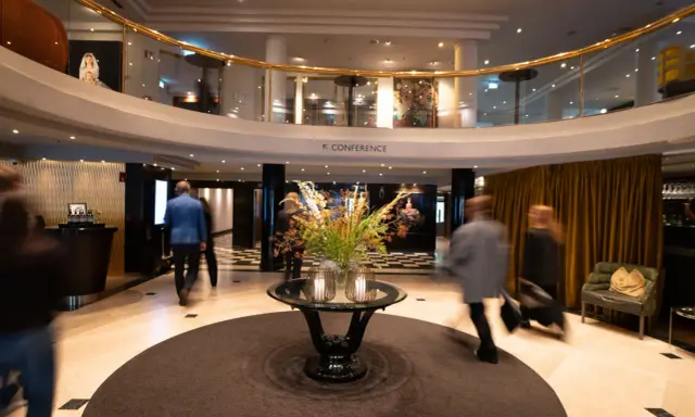 Elegant hotell park lobby med en blomsterdekor i mitten. Människor rör sig förbi i en suddig rörelse.