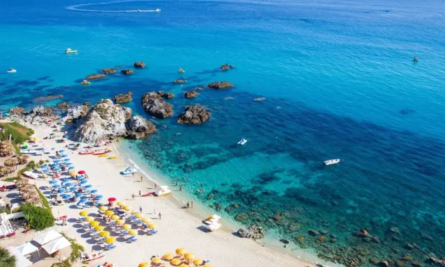 Spiaggia calabrese con ombrelloni colorati e mare cristallino, ideale tra i posti da visitare in Calabria con bambini per una vacanza indimenticabile.