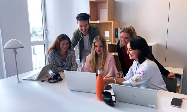 Zespół młodych ludzi pracuje razem przy biurku w biurze Alstom Wrocław, śmiejąc się i patrząc na ekran laptopa.