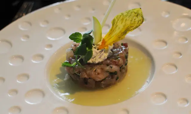 Un tartare de poisson finement préparé, garni de crème, herbes fraîches et d'une fleur jaune, une des spécialités Limoges.