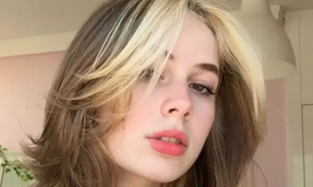 Dziewczyna z burzą blond i brązowych włosów w stylu curly wolf cut, z pasemkami przy twarzy.
